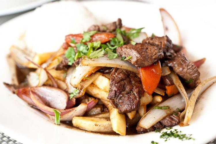 Un plato con lomo saltado, carne y verduras salteadas con paatas fritas y una salsa sabrosa.