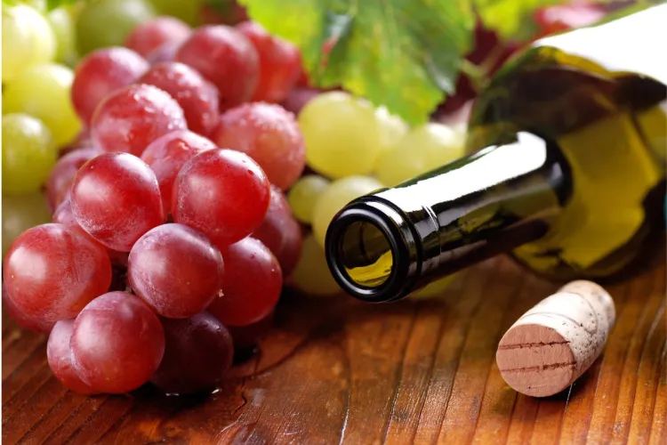 Botella de vino abierta al lado de uvas blancas y uvas tintas.