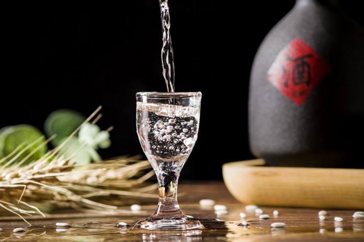 Un chorro de licor blanco chino, baijiu, llenando una copa transparente, con una botella de cerámica detrás que supuestamente también contiene este tipo de licor. 