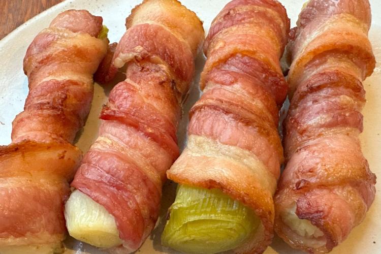 Puerros cocidos y después horneados con panceta ahumada.