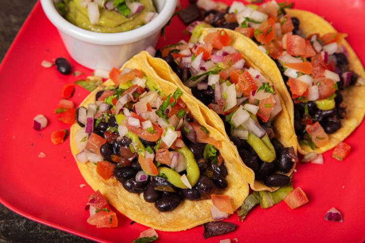 Tres tacos de alubias negras acompañados de salsa.