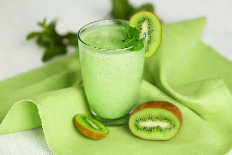 Un vaso con batido de kiwi, decorado con una rodaja de kiwi y unas hojas de menta, sobre una servilleta de color verde claro.