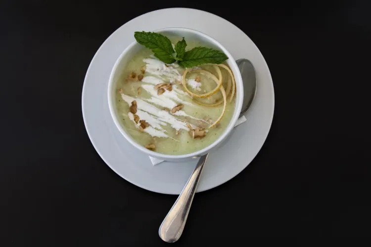 Un cuenco con gazpacho de melón decorado con menta, nata líquida y nueces.