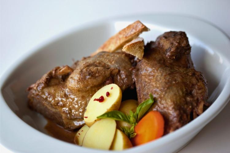 Pichón guisado con verduras en un plato hondo de loza blanca.
