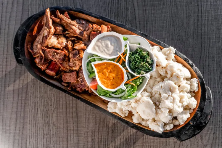 Plato suazi con carne a la parrilla, o braai, a la izquierda, pap blanco a la derecha, con verduras, ensalada y salsas en el centro.