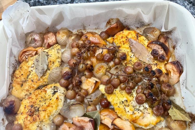 Pechuga de pollo con uvas y manzana en una fuente de horno forrada con papel encerado.