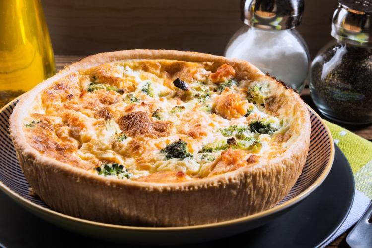 Una quiche de salmón ahumado y brócoli fotografiada en un entorno rústico.