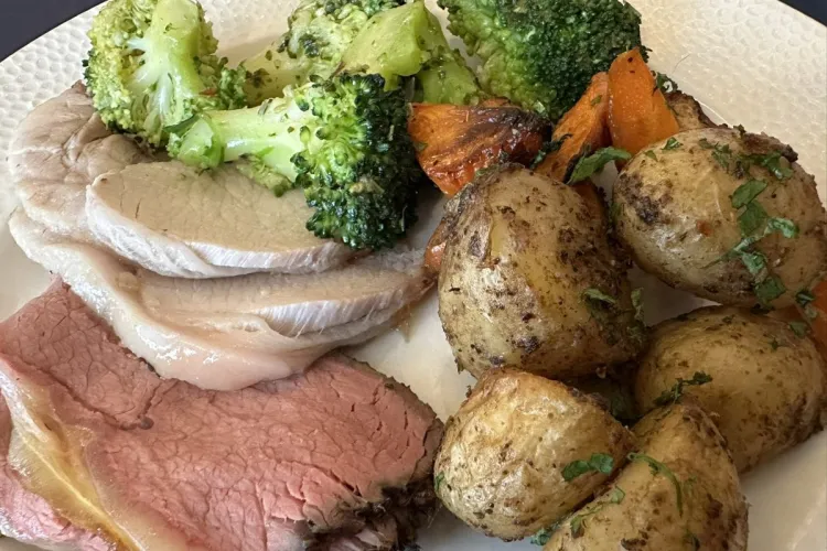 Un plato con lonchas de rosbif y de cerdo asado con guarnición de brócoli, zanahorias y patatas asadas.