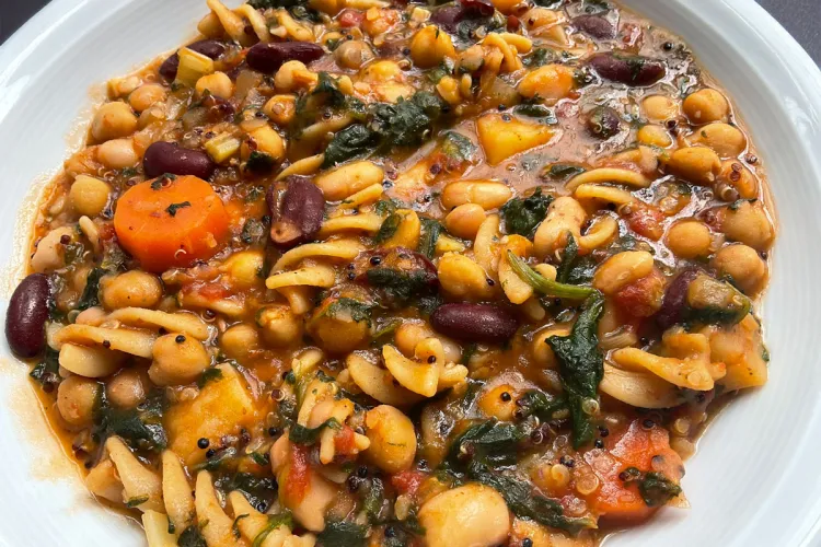 Un plato hondo con una porción generosa de una sopa con legumbres, pasta y verduras.
