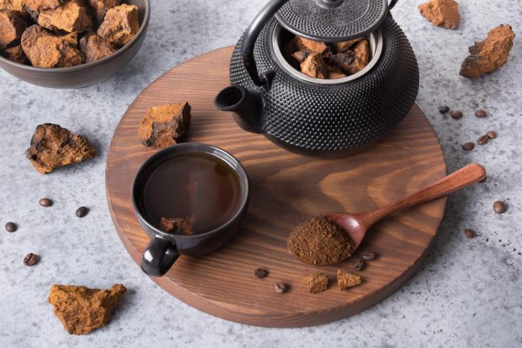 Una taza de té de hongo chaga con tetera, trozos de chaga secos y polvo sobre una tabla de madera.