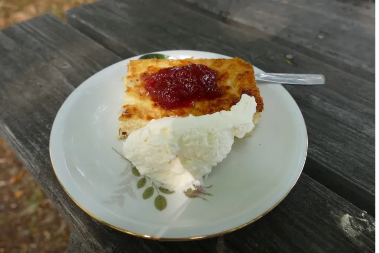 Un trozo de pastel de queso sueco, ostkaka, servido con mermelada de frutos rojos y nata montada.