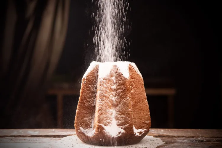 Pandoro italiano en forma de estrella, siendo decorado con azúcar glas espolvoreado sobre su superficie dorada.