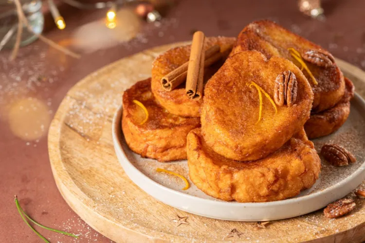 Rabanadas brasileñas o portuguesas doradas, servidas en un plato, decoradas con corteza de cítricos y pacanas.