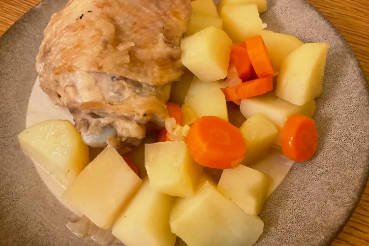Un plato de pollo guisado a la cerveza con guarnición de patatas y zanahorias guisadas.