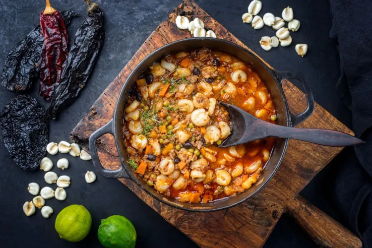 Un cuenco de pozole rojo rodeado de algunos de los ingredientes que se usan para hacerlo.