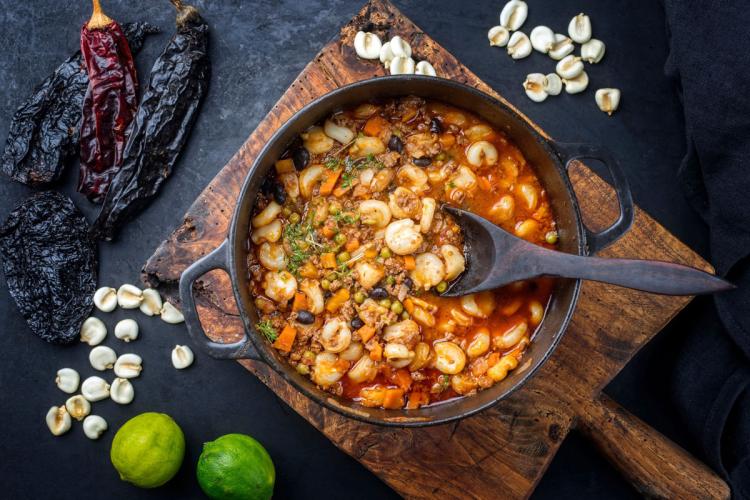 Un cuenco de pozole rojo rodeado de algunos de los ingredientes que se usan para hacerlo.