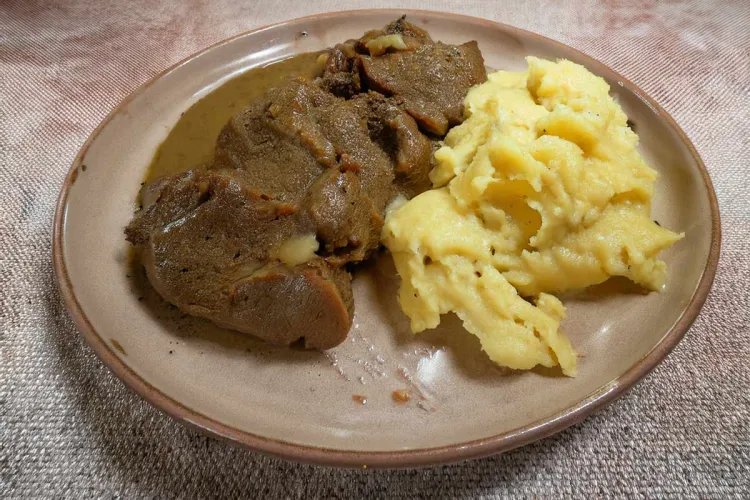 Un plato con carne guisada con su salsa de aceitunas y puré de patata.