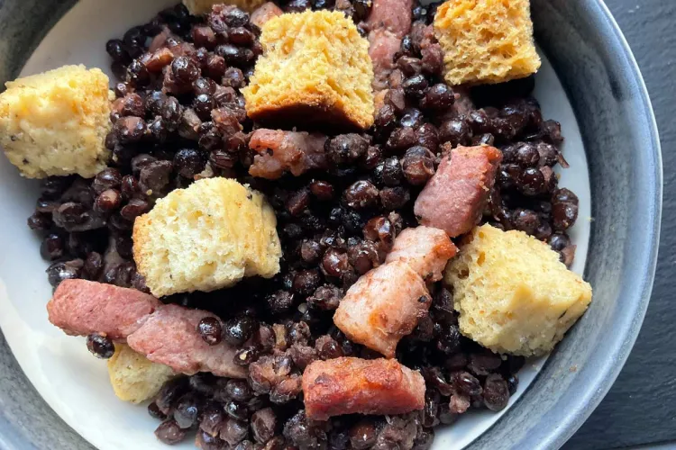 Un plato hondo con lentejas a la Villalar con guarnición de cuscurros de pan.