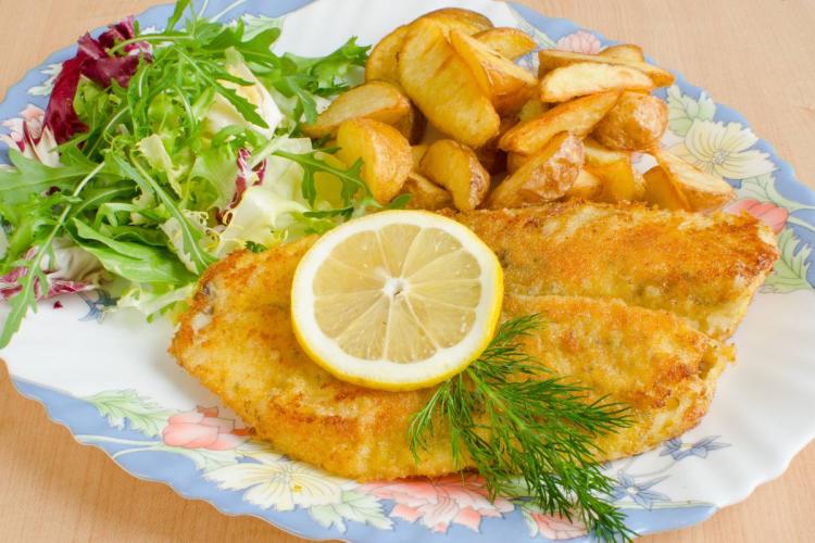 Filetes de tilapia empanados con patatas fritas, adornados con hierbas y limo2n.