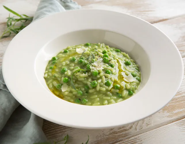 Un arroz al estilo italiano de guisantes y estragón servido en plato hondo blanco.