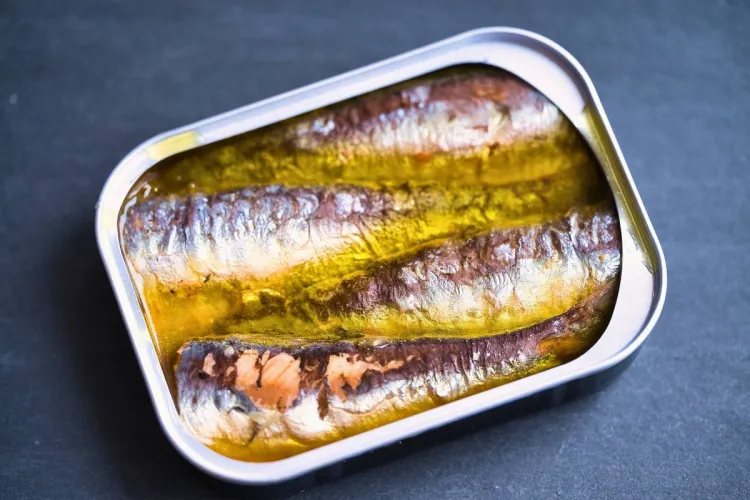 Una lata, abierta, de sardinas en aceite sobre una superficie de pizarra negra.