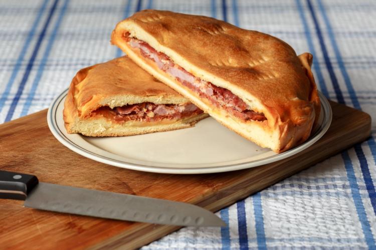 Hornazo cortado por la mitad con relleno de embutido, sobre plato y tabla de madera.