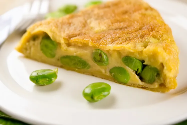 Porción de tortilla española de habas tiernas en un plato blanco.