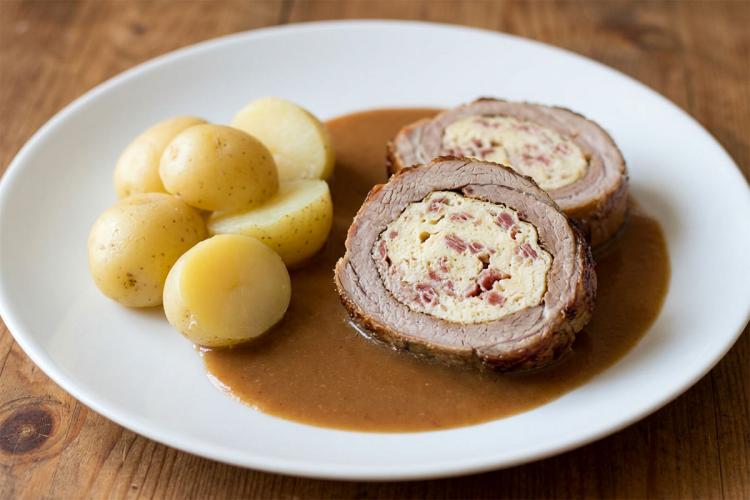 Plato con dos rodajas de ternera rellena de tortilla con jamón, acompañadas con su salsa y patatitas al vapor.