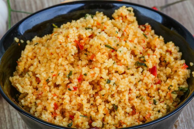 Cuscús especiado con tomate picado y cebollino servido en un cuenco negro.
