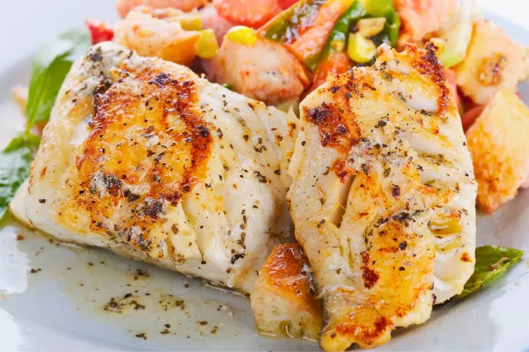 Dos filetes de pescado, dorad o mahi-mahi, a la parrilla con hierbas, acompañados de verduras y pan tostado en un plato.