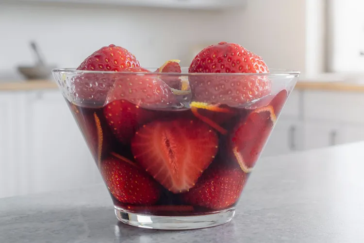 Un recipiente con fresas al vino tinto con piel de naranja finamente cortada - imagen sintética.