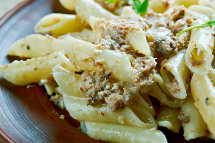 Pasta con sardinas servida en un plato marrón, con sardinas desmenuzadas en la salsa y unas hojas verdes como decoración.