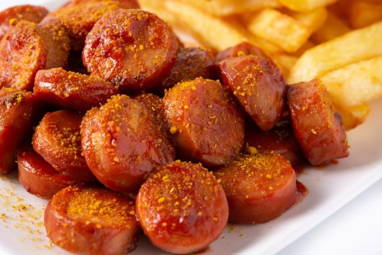 Salchicha alemana al curry, o currywurst, cortada en rodajas y acompañada con patatas fritas