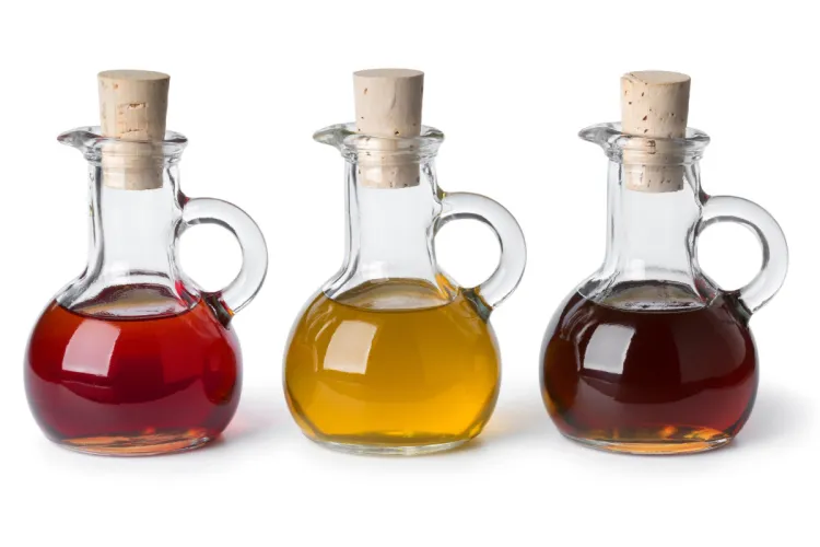 Tres aceiteras de cristal con tapón de corcho, con aceites de cocina de color rojizo, dorado y ámbar oscuro, sobre fondo blanco