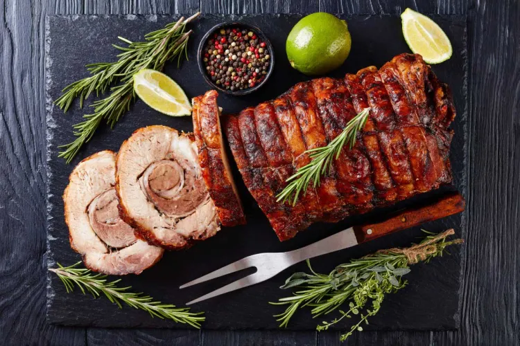 Asado de cerdo enrollado y dorado, parcialmente cortado en lonchas y acompañado de romero, lima y pimienta.