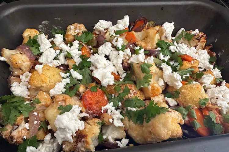 Bandeja de horno con coliflor asada, zanahoria, garbanzos y cebolla, cubierta con queso feta desmenuzado y cilantro fresco