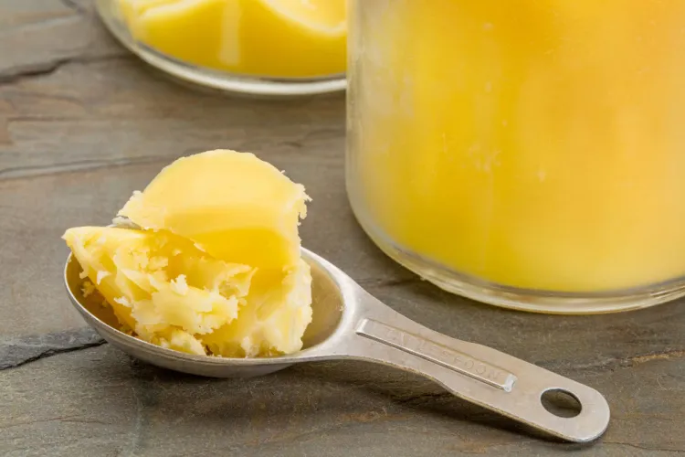 Cuchara con ghee cuajado de color amarillo junto a un tarro de cristal con ghee derretido