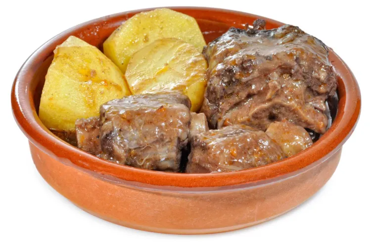 Cazuela de barro con trozos de patata y rabo de toro guisados en su salsa.