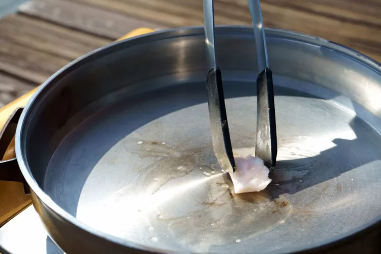 Trozo de sebo de vacuno sujeto con unas pinzas para engrasar una sartén de acero al aire libre