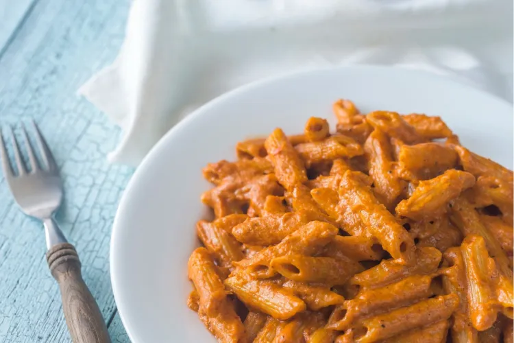 Penne con salsa cremosa de tomate (pasta a la vodka) en un plato blanco, con un tenedor sobre una mesa de madera azul clara