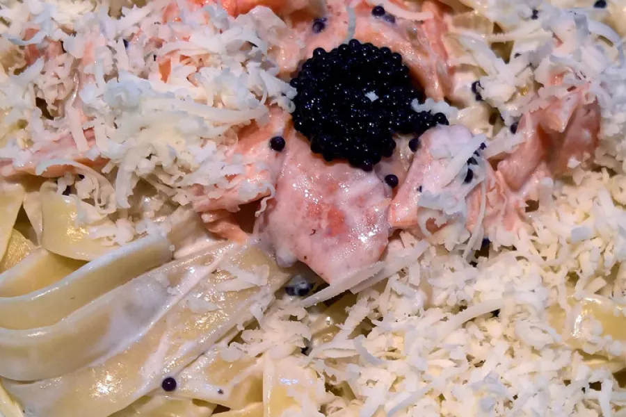 Detalle de pasta con salmón ahumado y falso caviar espolvoreada con parmesano rallado.