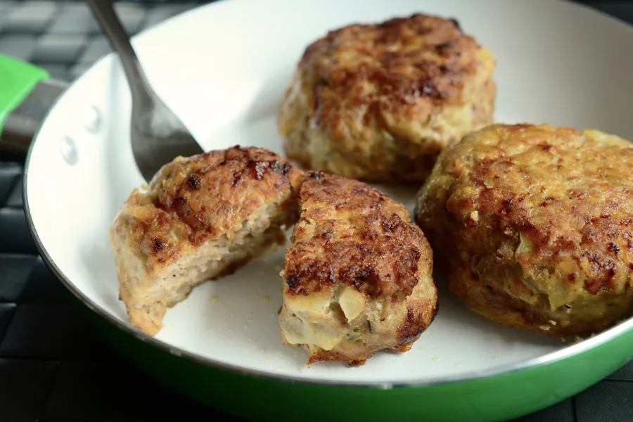 Tres albóndigas alemanas, frikadellen, en una sartén. Una de ellas partida por la mitad.