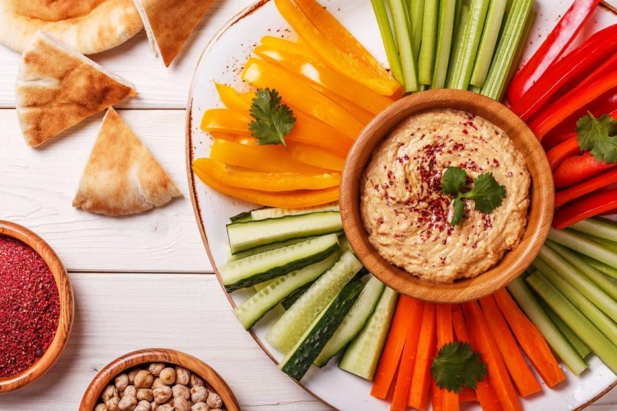 Hummus en un cuenco rodeado de verduras crudas cortadas en bastoncitos.