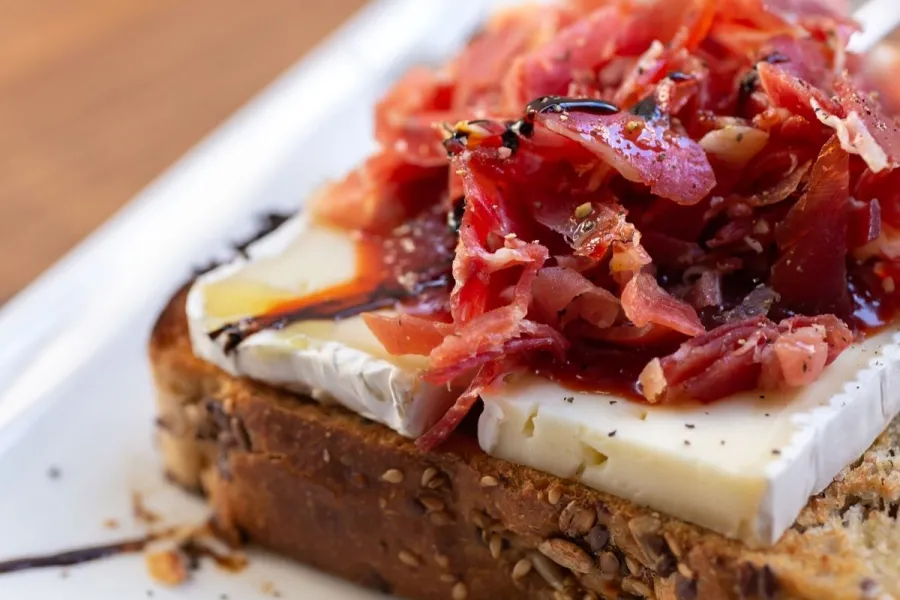 Tostada con queso brie, jamón serrano y confitura de tomate.