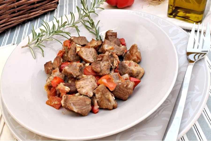 Cordero guisado en un plato con una rama de romero.