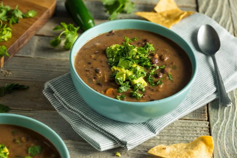 Sopa de frijoles negros adornada con aguacate y cilantro.