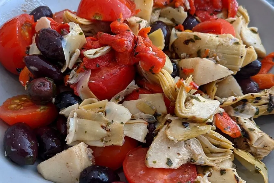 Ensalada de alcauciles con pimientos rojos, aceitunas y aliño a las hierbas.
