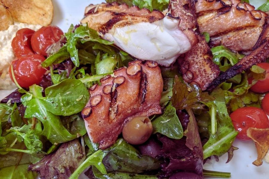 Ensalada compuesta con lechuga, tomate, pulpo, aceitunas, humus y aceite de oliva.