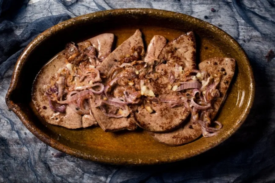 Cuatro filetes de hígado encebollado en una fuente de barro.