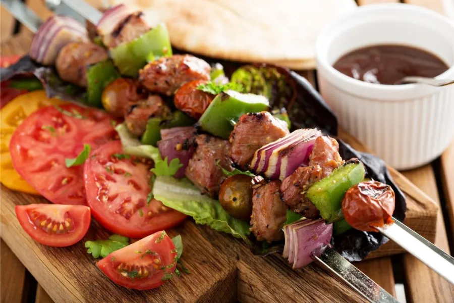 Pinchos de ternera acompañados de rodajas de tomate, salsa y pan plano.